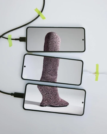 Three smartphones display parts of a textured leg on a white surface, connected by black cables and secured with green tape.