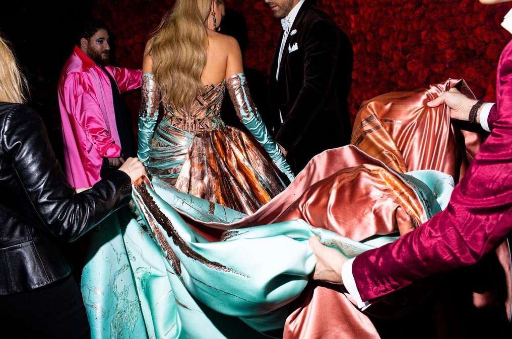 Fashionable group poses with a striking strapless gown, featuring ornate copper detailing and long turquoise gloves, amidst a textured rose background.