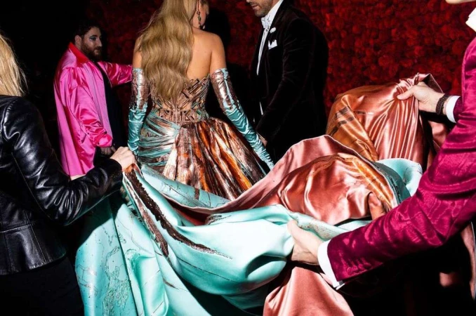 Fashionable group poses with a striking strapless gown, featuring ornate copper detailing and long turquoise gloves, amidst a textured rose background.