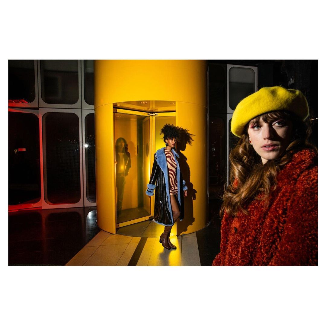 Three women showcase retro-inspired fashion with a yellow elevator as a backdrop, shot with bright studio lighting and a focus on vibrant colors.