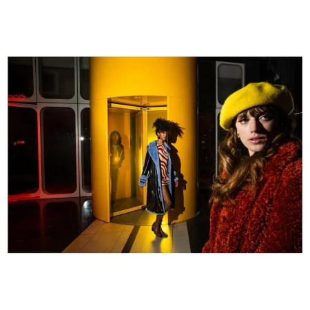 Three women showcase retro-inspired fashion with a yellow elevator as a backdrop, shot with bright studio lighting and a focus on vibrant colors.