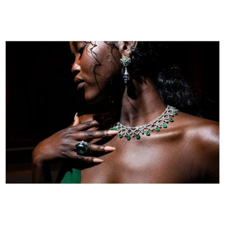 Elegant woman with jewelry: Close-up of a dark-skinned woman wearing emerald necklace, ring, and earrings, with a blurred black backdrop.