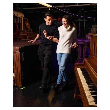 Hugh Jackman and Sutton Foster dancing playfully in a backstage rehearsal space with a piano.
