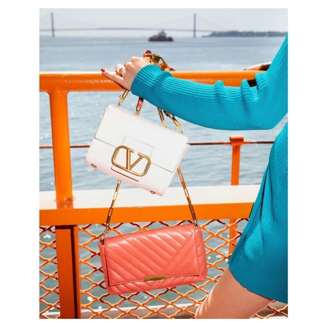 Two designer handbags, one white with a gold V logo and one salmon-colored with chevron stitching, are displayed on a ferry.