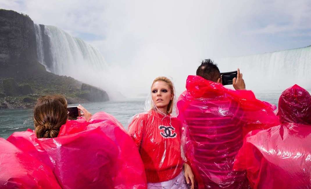Four people in raincoats pose near Niagara Falls; the woman in the center wears a red sweatshirt in a scenic, outdoor shot.