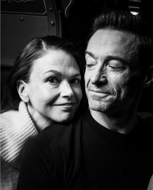 Black and white portrait of a smiling adult couple in an indoor environment; the man is winking at the camera.
