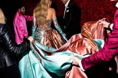 People in formal attire holding the large turquoise and copper silk train of an ornate gown against a red floral wall