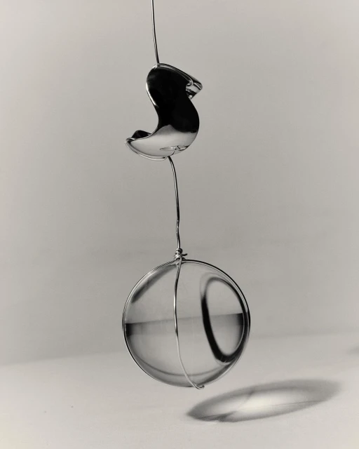 Still life of a clear glass sphere hanging from a thin wire against a gray gradient background with diffused lighting.