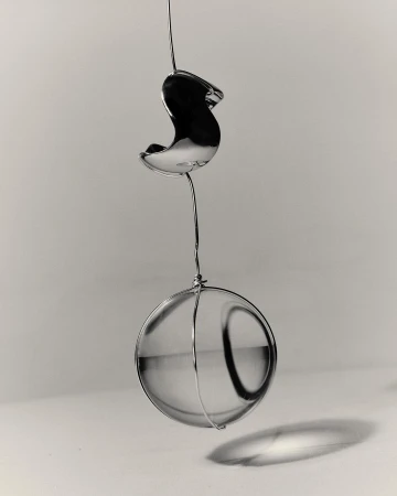 Still life of a clear glass sphere hanging from a thin wire against a gray gradient background with diffused lighting.
