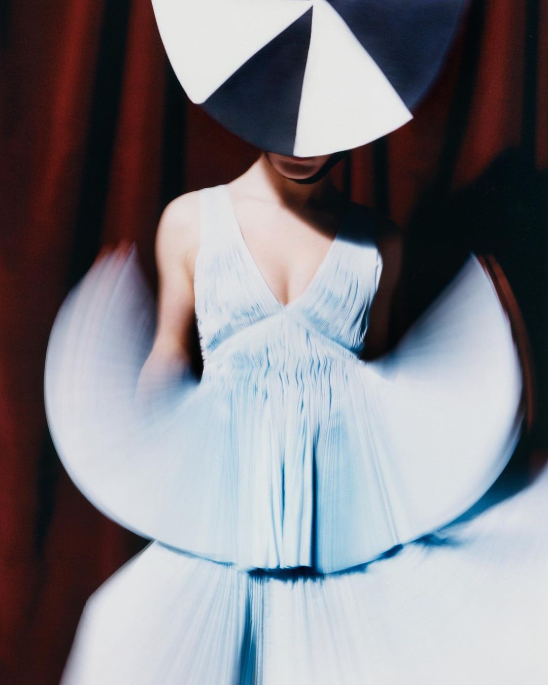 Fashion shot: Woman in a light blue dress and black and white hat poses in front of red curtains with motion blur effect.