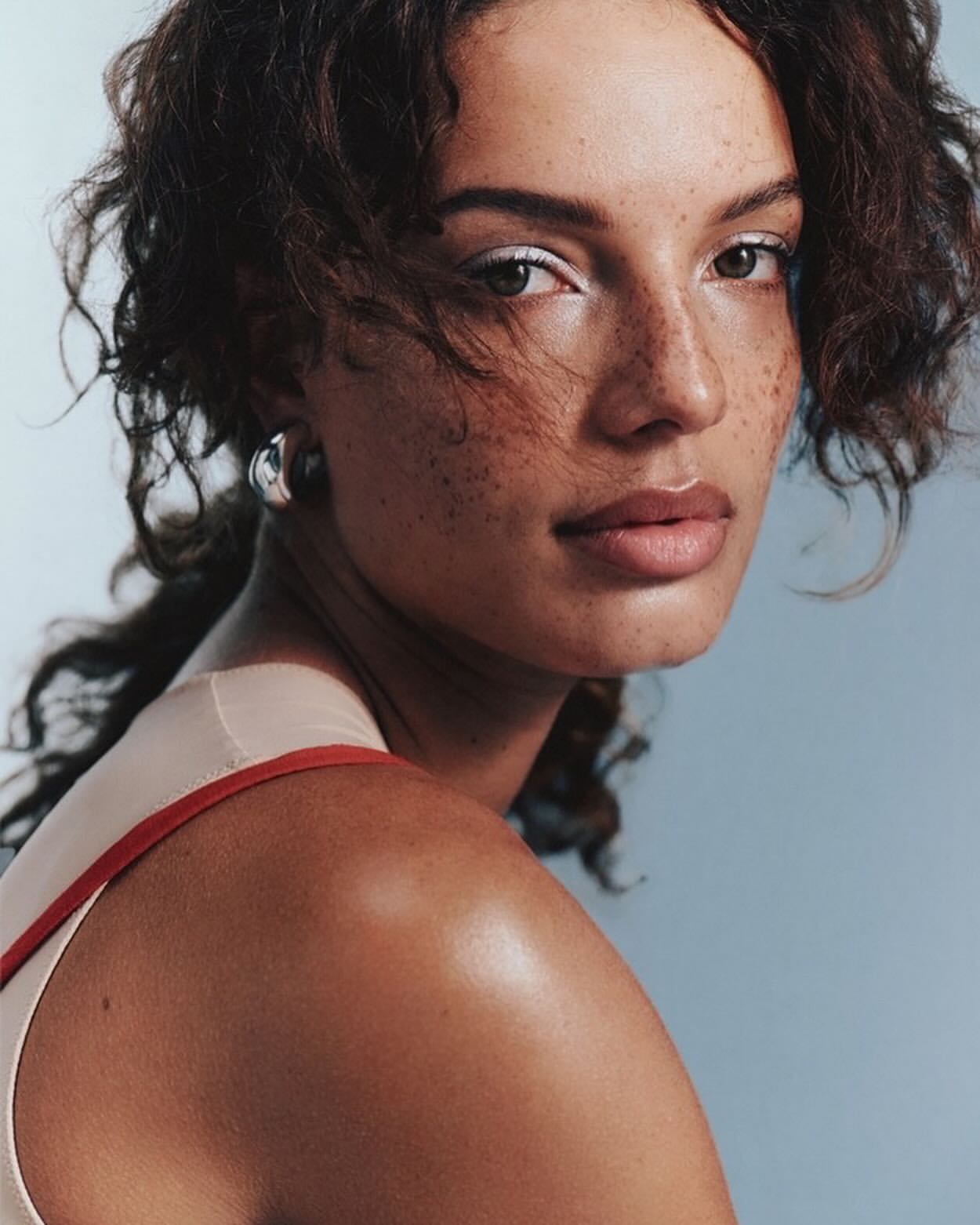 Close-up portrait of a woman with curly brown hair, freckles, and silver hoop earrings, captured by photographer Lara Angelil