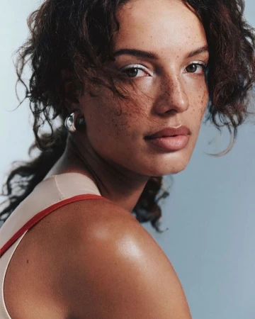 Close-up portrait of a woman with curly brown hair, freckles, and silver hoop earrings, captured by photographer Lara Angelil
