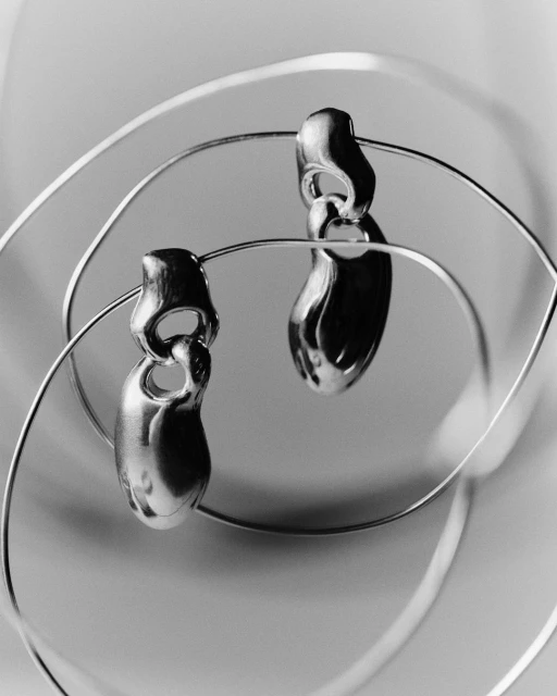 Elegant, shiny silver earrings on a thin, coiled wire. The studio shot showcases a modern jewelry design against a neutral backdrop.