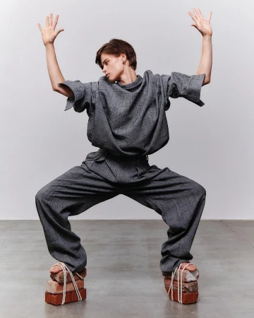 Fashion-forward individual strikes a pose in matching gray ensemble, unconventional brick footwear, set against a neutral backdrop. 