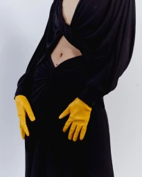 Model in a black dress with a plunging neckline wearing bright yellow leather gloves against a white background.