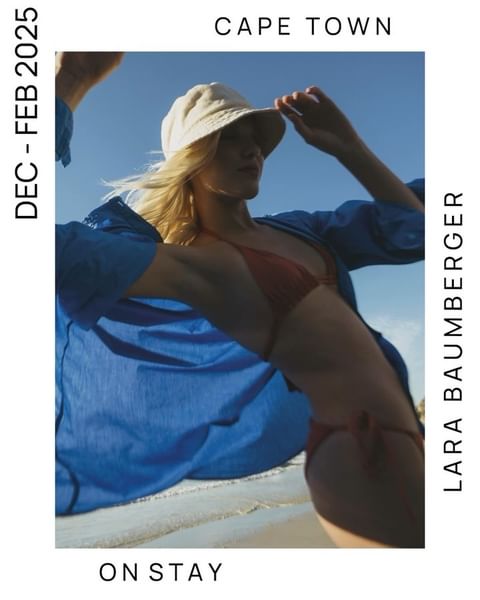 A woman in a rust-colored bikini and blue shirt poses on a beach under a blue sky, wearing a bucket hat in a fashion editorial.