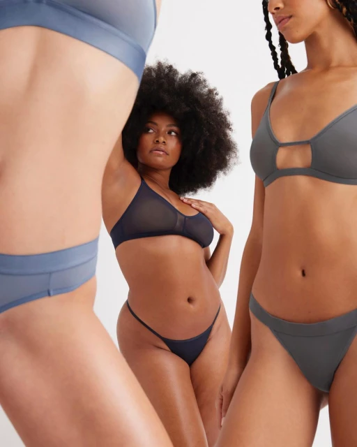 Three women pose in blue and gray lingerie sets against a white backdrop, showcasing fashion and beauty in a studio setting.