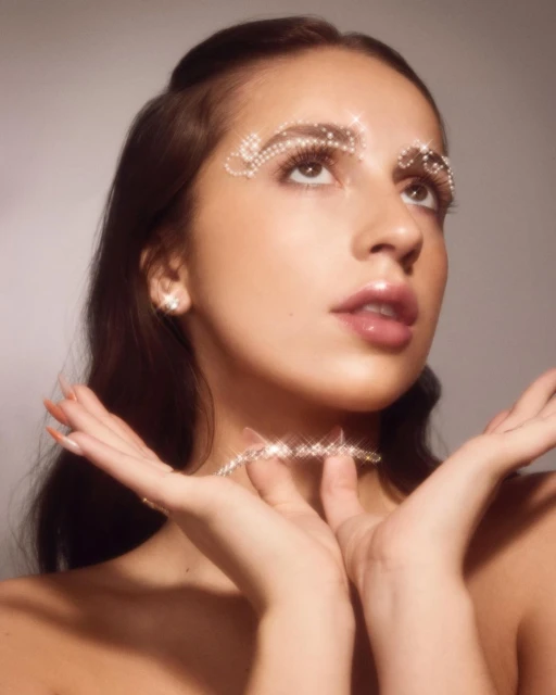Close-up portrait of a young woman wearing decorative jewelry around her eyes and neck. She is looking up with her hands raised.