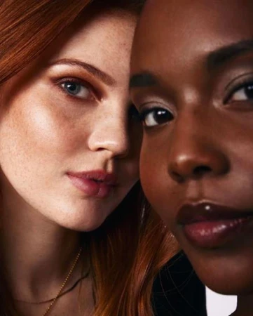 Close-up portrait of two female models with distinct facial features posing close together against a neutral background.