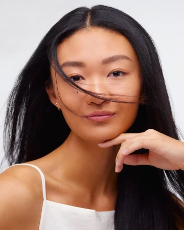 Close-up portrait of an East Asian woman with long dark hair, wearing a white top against a clean background, photographed by Lara Callahan.
