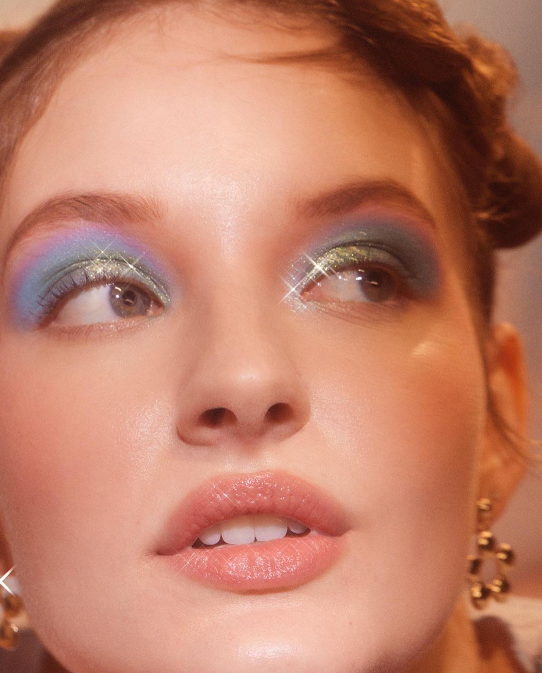 Close-up portrait of a woman wearing colourful eyeshadow and glitter with updos by photographer Lara Callahan