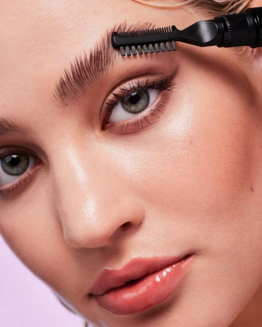 Close-up of a fair-skinned adult woman using a cosmetic brush on her eyebrow with a light purple background, beauty concept.