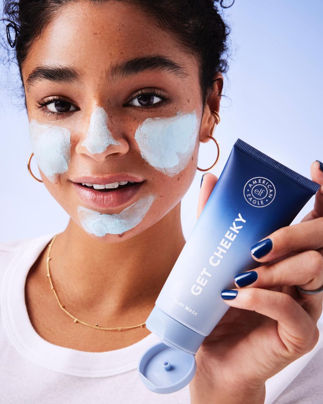 Young woman with blue facial mask applying cosmetic cream. Focus on skincare and treatment for a fresh, healthy complexion.
