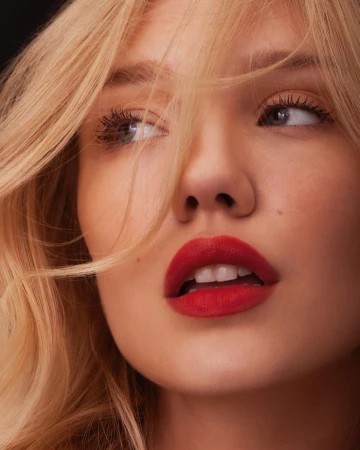 Close-up beauty portrait of a blonde woman with vibrant red lipstick and strands of hair falling across her face by Lara Callahan.