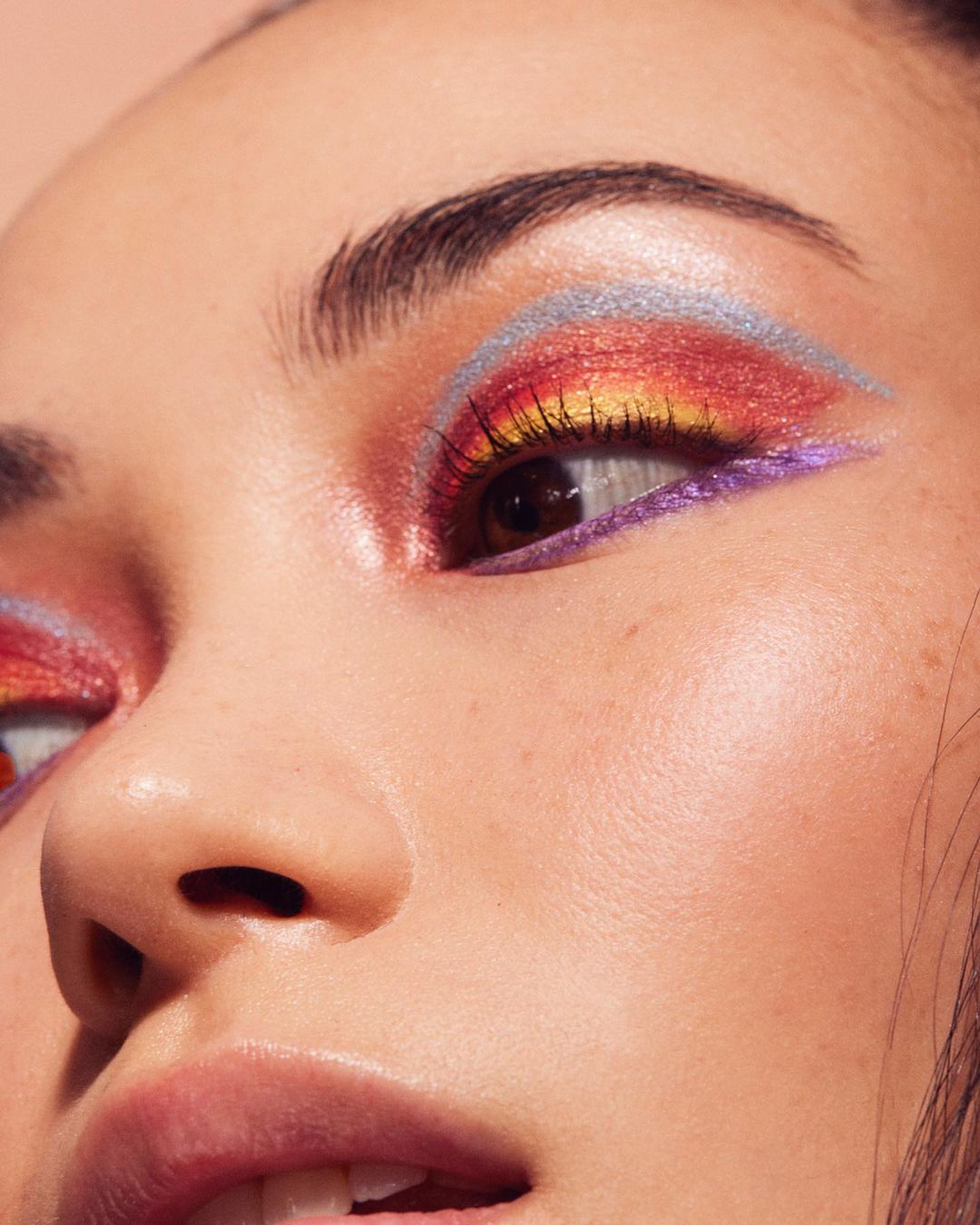 Close-up of a woman's face, emphasizing colorful and artistic eye makeup in shades of red, yellow, and blue.