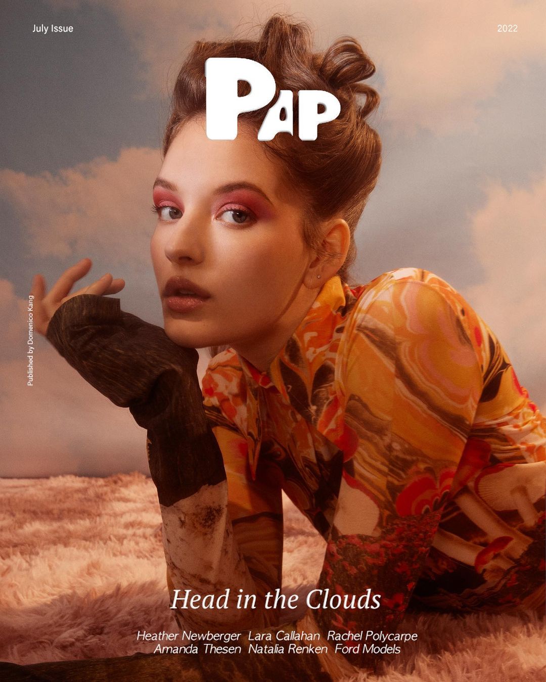 Magazine cover featuring a young woman with pink eye makeup and patterned clothing posing against a dreamy sky backdrop.