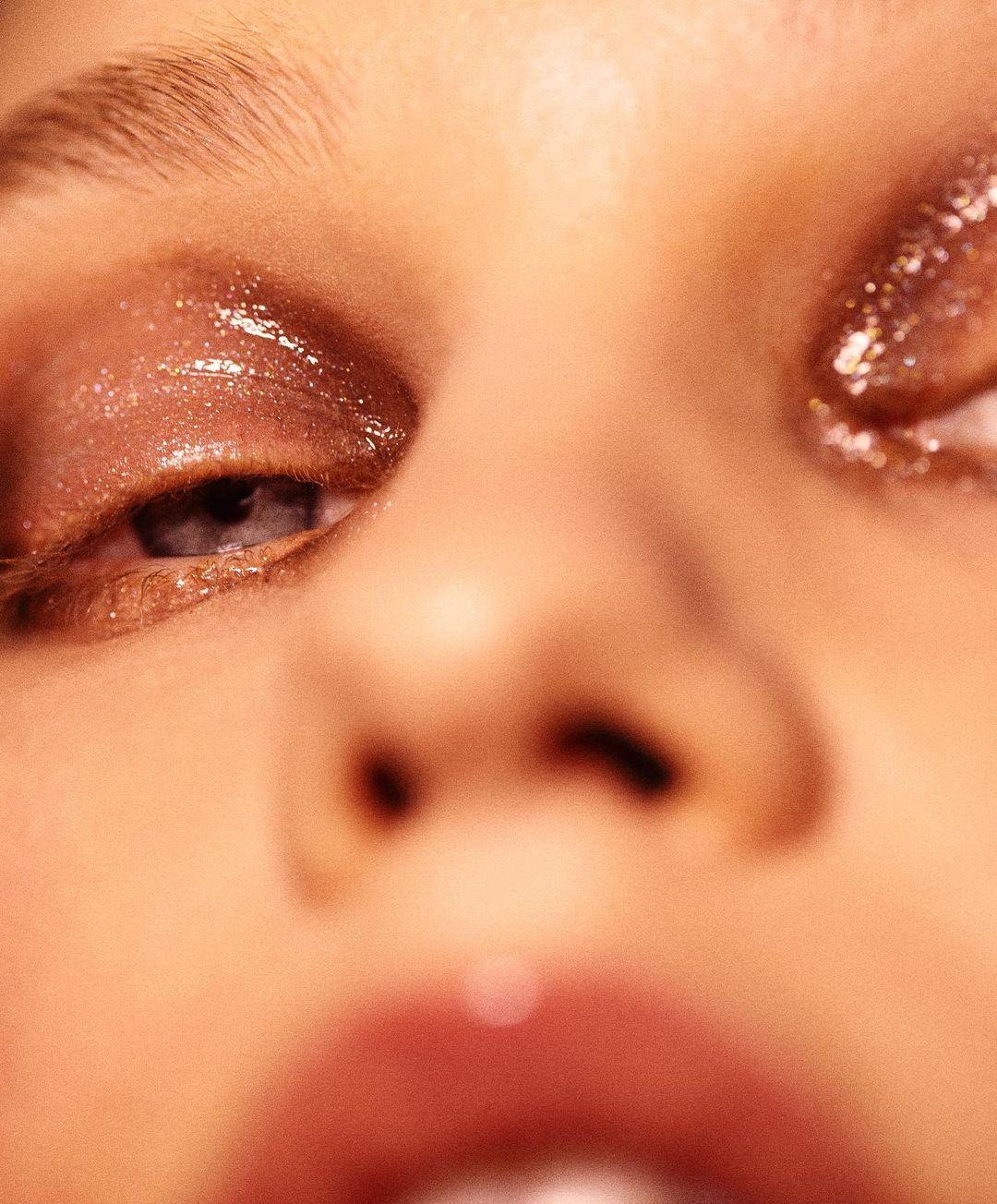 Close-up of a woman's face features glossy eye makeup. The focus is on her eyes and the shimmering effect of the makeup.
