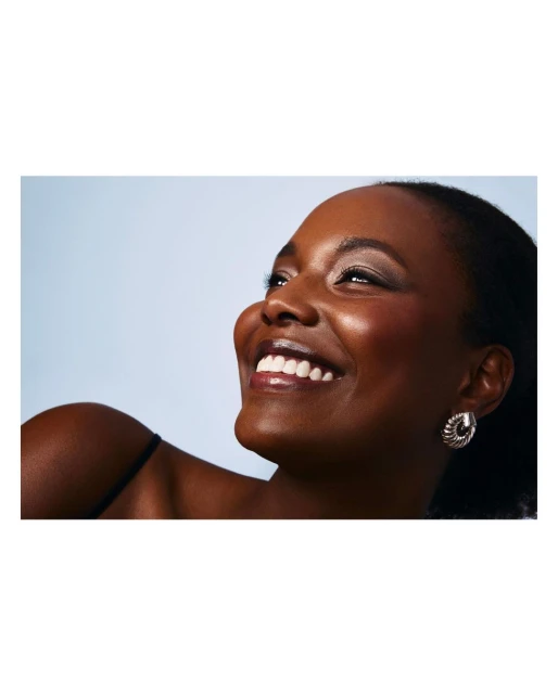 Close-up portrait of an African-American woman smiling and looking upwards with a light blue background and wearing decorative earrings.
