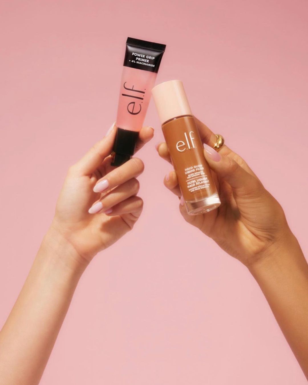Two e.l.f. makeup products, a primer and a liquid filter foundation, held up by two tan-skinned adult female hands against a pink background.