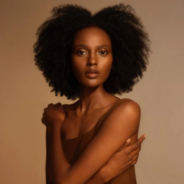 Close-up studio portrait of a serene Black woman with crossed arms and dark brown hair, set against a warm beige background.