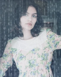 Portrait of a young woman in a floral dress shot through a textured mesh or screen by photographer Lara Rossignol.
