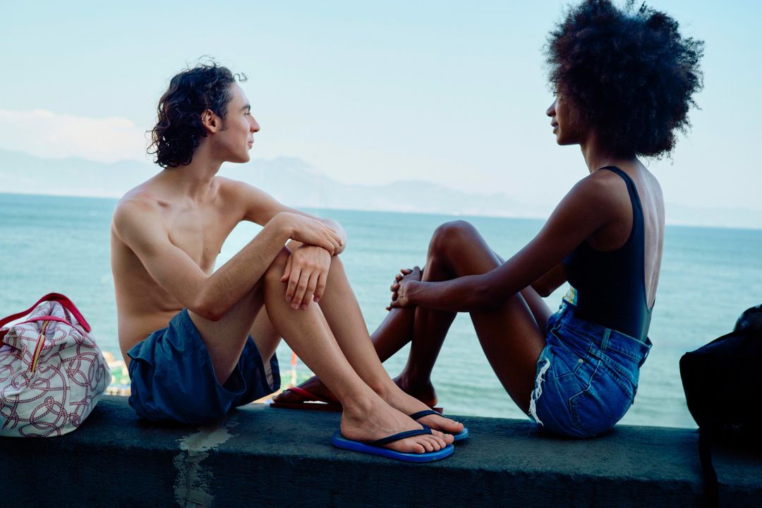 Two young adults sitting together on a concrete wall overlooking the ocean, captured by photographer Lars Borges.