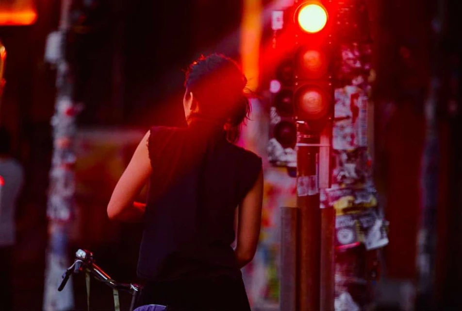 Woman in black top standing next to a glowing red traffic light at night by photographer Lars Borges