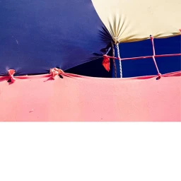 Close-up abstract view of taut pink, navy blue, and cream fabric tensioned with red ties against a bright blue sky.