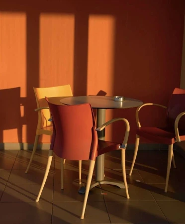 Round cafe table surrounded by three chairs against a warm terracotta wall with strong afternoon shadows