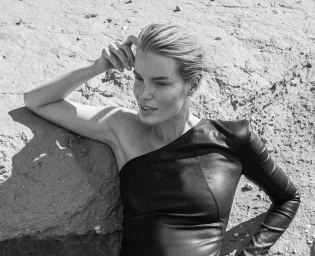 Monochrome portrait of a woman in a black leather dress leaning against a rocky terrain by Lars Botten