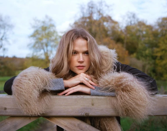 Woman resting her chin on her hands over a wooden fence outdoors in a park