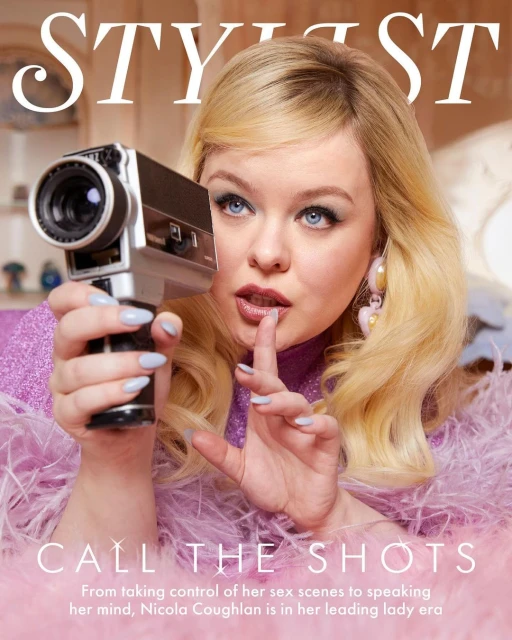 Nicola Coughlan cover shot, holding an old-fashioned film camera in a photo studio with a pink feather boa and blonde hair.