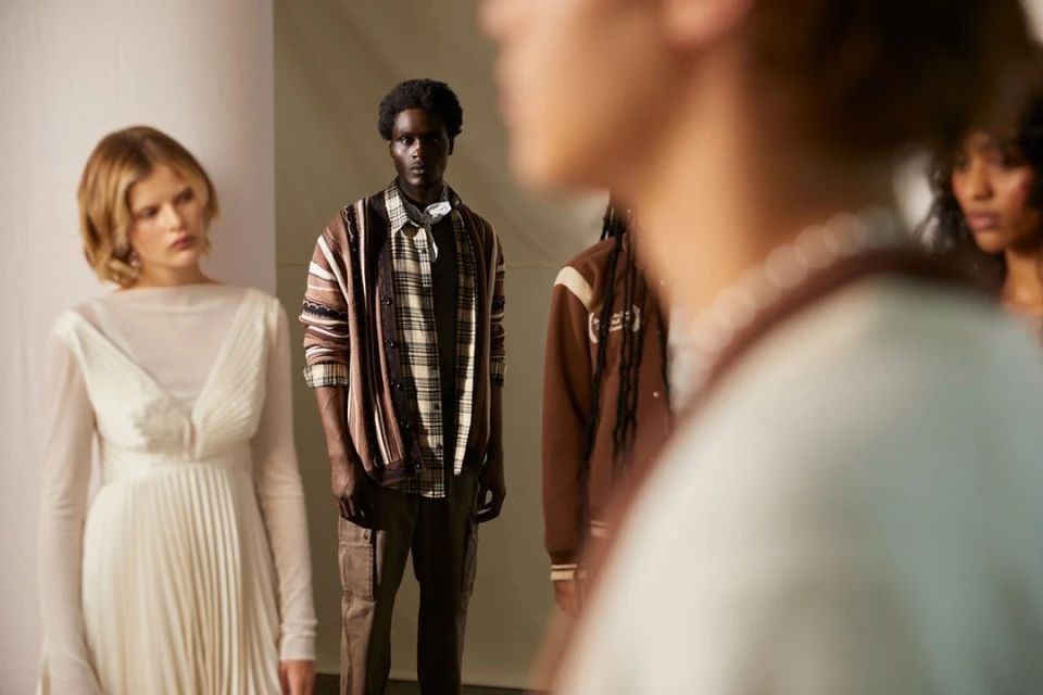 Fashion models showcase neutral-tone outfits in a studio setting. A diverse group of adults is captured with soft lighting and a neutral background.