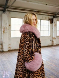 Blonde woman wearing a leopard print coat with pink fur collar standing in a loft space