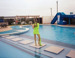 Woman in bright green dress and oversized sunglasses posing by an outdoor swimming pool by Laura Allard-fleischl