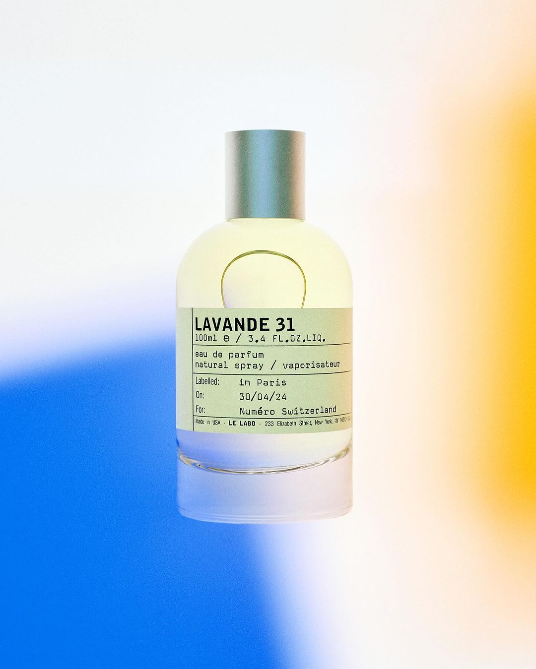 Perfume bottle of Lavande 31 by Le Labo, with minimalist design, stands against a vibrant background of blue, white, and yellow hues.