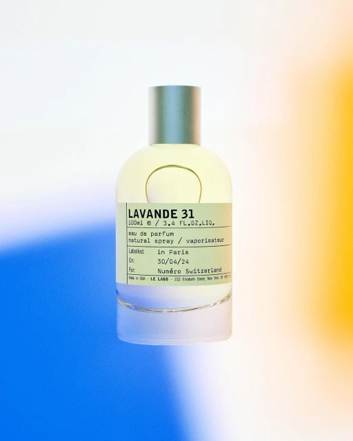Perfume bottle of Lavande 31 by Le Labo, with minimalist design, stands against a vibrant background of blue, white, and yellow hues.
