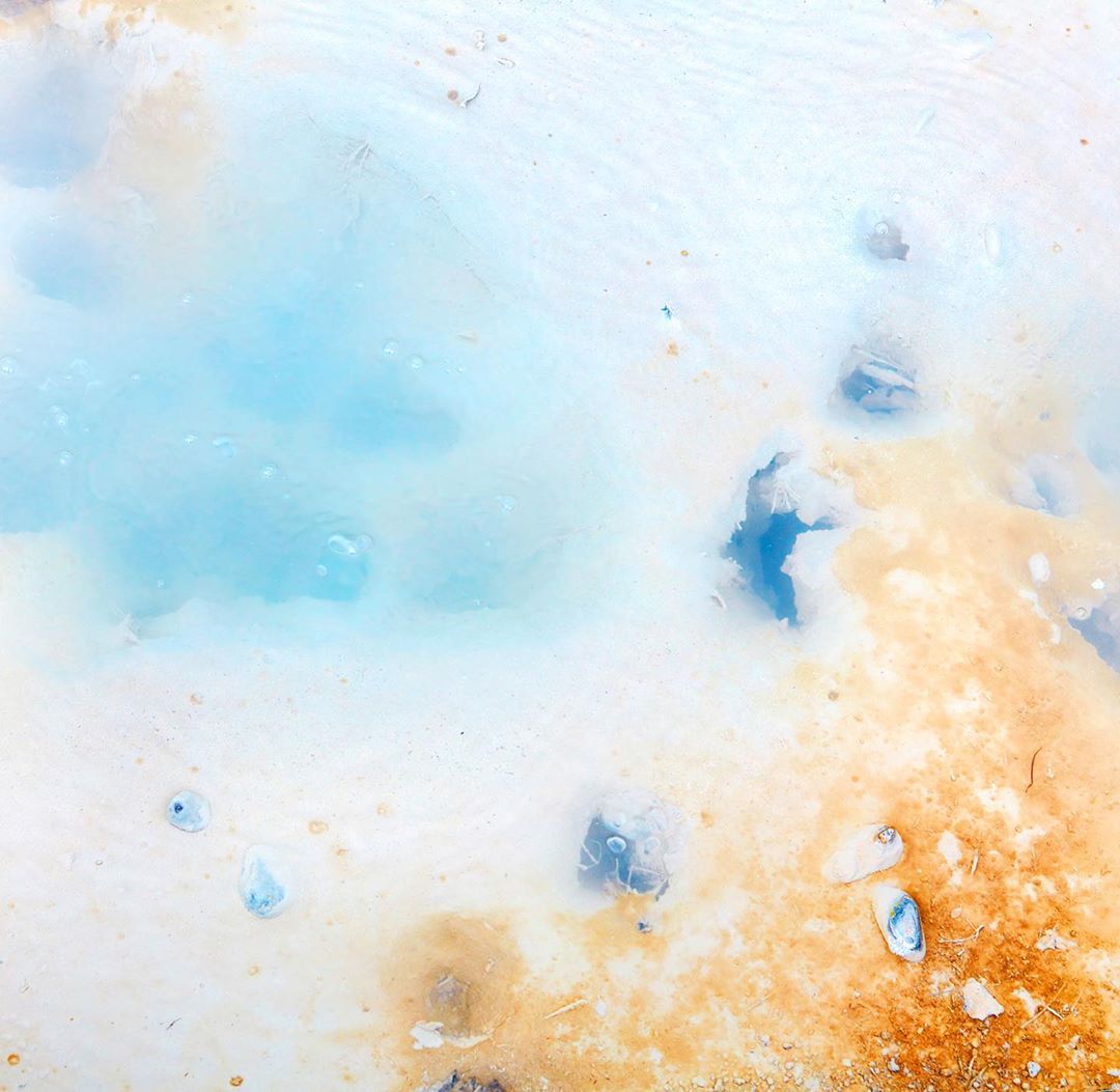 Abstract landscape with mineral pool featuring light blue water surrounded by beige and white earth, textures, and varied visual patterns.