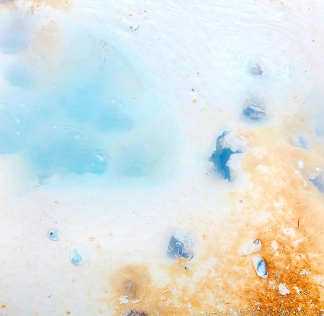 Abstract landscape with mineral pool featuring light blue water surrounded by beige and white earth, textures, and varied visual patterns.