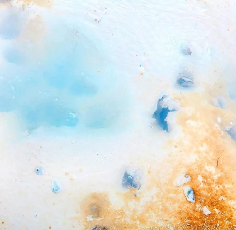 Abstract landscape with mineral pool featuring light blue water surrounded by beige and white earth, textures, and varied visual patterns.